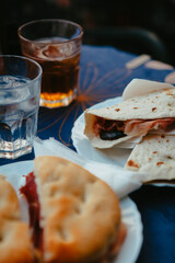 Traditional Italian food. Crispy panini and piadina sandwiches with prosciutto (speck), cheese, lettuce and vegetables with fresh drinks on a table with a blue tablecloth. Healthy European snack.