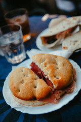 Traditional Italian food. Crispy panini and piadina sandwiches with prosciutto (speck), cheese, lettuce and vegetables with fresh drinks on a table with a blue tablecloth. Healthy European snack.