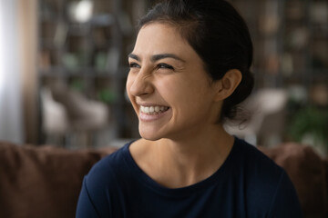 Close up of excited millennial Indian woman look in distance laugh at funny joke. Smiling young mixed race ethnicity female have fun dream or think of future success perspectives. Humor concept.