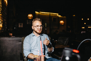 young man smokes a hookah in the evening in a hookah bar.