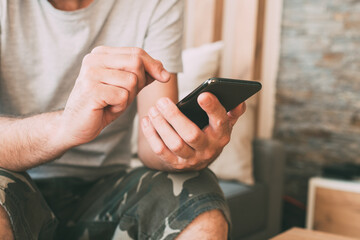 Close up of casual male hands using mobile smart phone at home in privacy of his living room