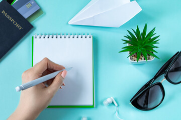 A woman is planning a summer vacation. Travel accessories on a blue background. Passport, sunglasses and notepad.