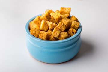 Square-shaped bread crumbs in a blue pot on a white background. Oven-fried golden brown bread crumbs. Close-up.