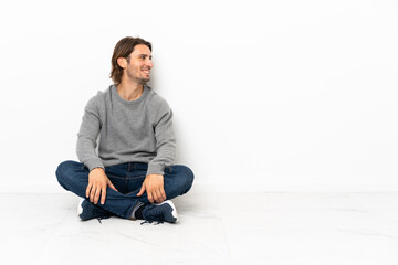 Young handsome man sitting on the floor over isolated background looking side