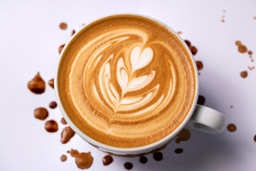 Cup of coffee with a rosette decoration surrounded by few brown drops on white background