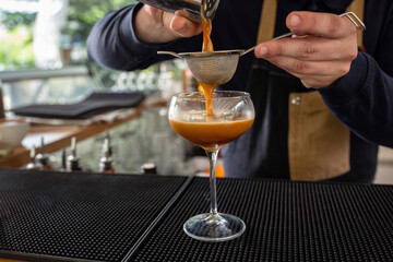Bartender using a strainer to separate cocktail ingredients as he pours a drink in the glass