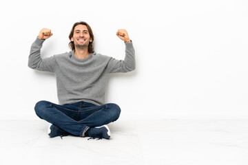Young handsome man sitting on the floor over isolated background doing strong gesture