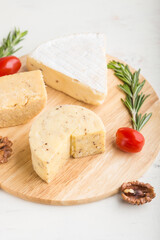 Cheddar and various types of cheese with rosemary and tomatoes on wooden board on a white background . Side view, selective focus.