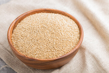 Wooden bowl with raw white quinoa seeds and wooden spoon on a gray concrete  background. Side view, selective focus.