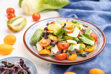 Vegetarian salad of pac choi cabbage, kiwi, tomatoes, kumquat, microgreen sprouts on a white concrete background. Side view, selective focus.