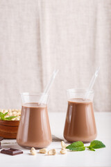 Organic non dairy cashew chocolate milk in glass and wooden plate with cashew nuts on a gray concrete background.