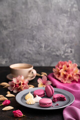 Purple macarons or macaroons cakes with cup of coffee on a black concrete background. Side view, selective focus, copy space.
