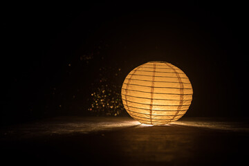 Beautiful paper lantern glowing on wooden table in dark.