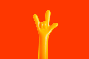 Photo of a plastic yellow colored hand sign gesture meaning I love you on orange background.