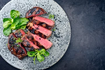 Fototapete Rund Modern style traditional barbecue dry aged wagyu rib-eye beef steaks with lambs lettuce and black salt sliced and served as top view in a Nordic design plate on a black board with copy space right © HLPhoto