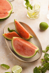 Watermelon slices, lime and mint in the morning light on sand-colored surface