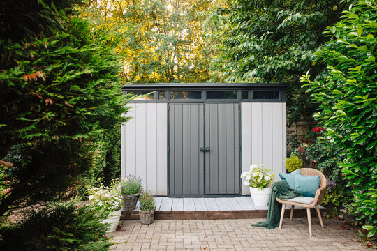 Gray Garden Shed In Summer. Lots Of Pots Of Flowers Next To A Plastic Garden Shed. Relax In The Garden. Big Garden In Germany 