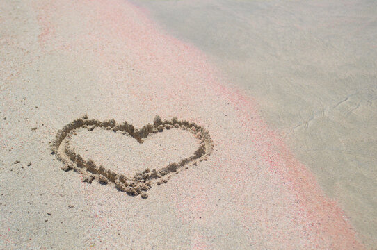 The heart as a symbol of love is painted on the white and pink sand.