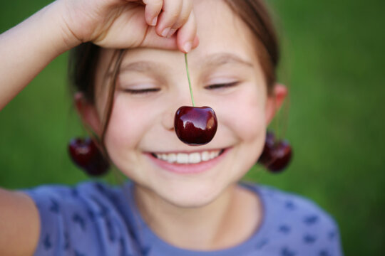 Pretty little girl with cherry earrings on green background