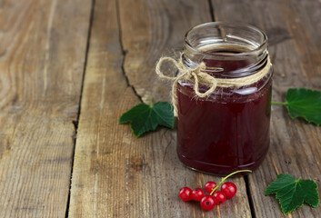 Red currant jam in a glass jar on wooden background
