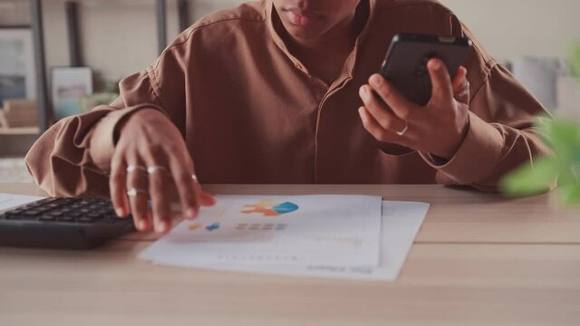 Close up young dark skinned woman summarizing monthly incomes and outcomes with calculator, checking electronic bills in e-banking application, managing expenditures and household money payments.