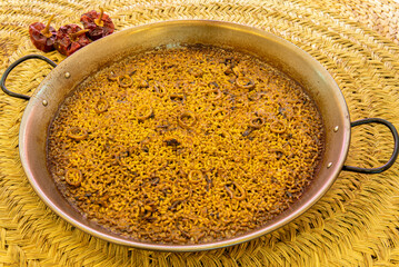 Rice paella with squid in a large paella pan on wicker trivets and dehydrated ñoras