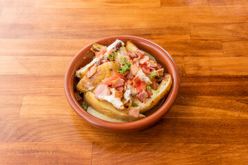 Roasted potato salad with skin, fried bacon in pieces, diced tomatoes with cream cheese on clay pot