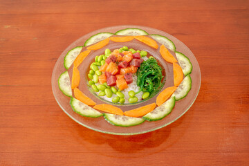 Curious presentation of poke bowl on a plate with cucumber and carrot slices, marinated salmon and red tuna tacos, edamame beans, wakame salad with sesame seeds and white rice as a base