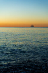 Fototapeta na wymiar Sunrise at sea with a frigate on the horizon