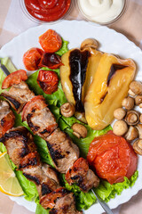 Pork shashlik on lettuce with baked tomatoes, mushrooms and peppers. Grilled meat on skewers. Lunch in nature