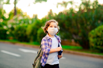 a schoolgirl is standing on the road in a plaid shirt and a medical mask, with a school backpack and a diary in her hands