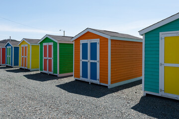 Fototapeta na wymiar A row of small colorful painted huts or sheds made of wood. The exterior walls are colorful with double wooden doors. The sky is blue in the background and the storage units are sitting on gravel.
