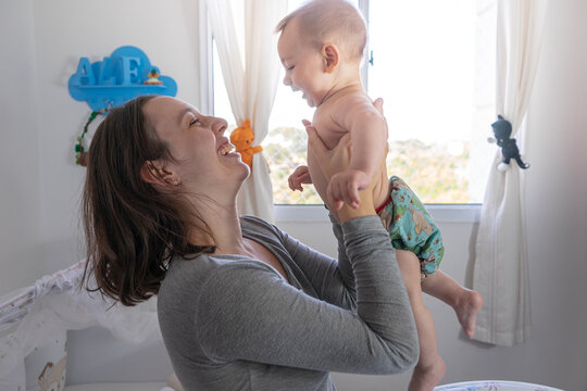 M&atilde;e brincando com beb&ecirc; na janela, jogando pra cima e rindo. Fraldas ecol&oacute;gicas