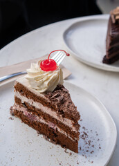 Slice of Decadent Black Forest Cake with Cream and a Cherry on Top on a Plate