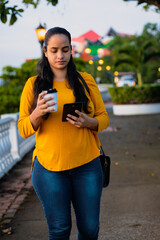 latin woman walking in the park with a glass of coffee and with the cell phone
