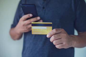 Man holding a credit card and using smart phone for online payment, using online banking application on his cell phone.