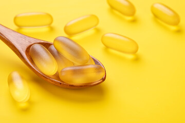 Wooden spoon with Omega 3 pills on yellow background. Supplement food vitamin D capsules. Close up