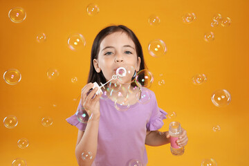 Little girl blowing soap bubbles on yellow background - Powered by Adobe