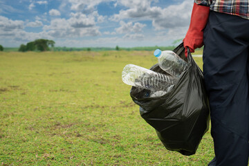 Man holding garbange plastic bottle on green field