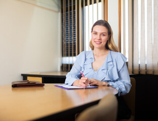 Smiling elegance business woman in office interior filling up documents