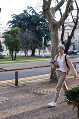 A A latin university student, walking in the city street. She is carrying folders in her hand and...