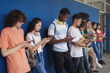 Group of multi-ethnic teenager friends using smart mobile phones in high school break - Concept of...