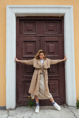 Fototapeta na wymiar Young millennial woman with wild hair dressed in an autumn coat posing near the door of an old building.