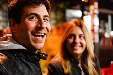 latin hispanic man with his partner in a city bar, man looking at camera laughing