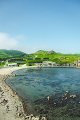 Fototapeta premium summer sea panorama. shallow, clear, transparent sea with reefs, rocks and and holiday houses on the green summer hills. Japan sea.