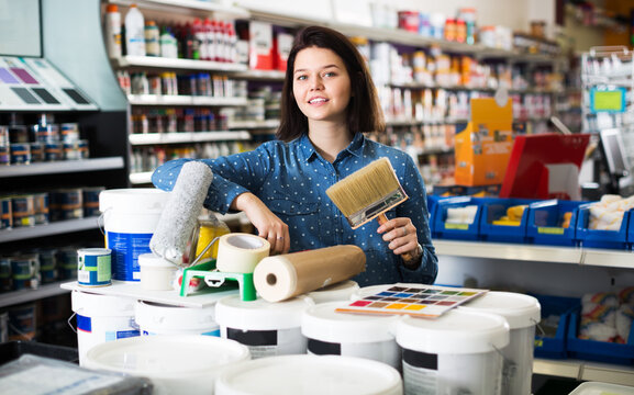 Young smiling woman buying tools for house decoration in paint supplies store