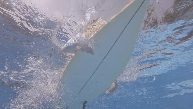Surfer man on surf board drifts on water on hot sunny day, bottom view, underwater shot.