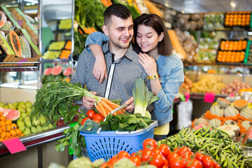 Man and woman are deciding on vegetables in grocery shop.