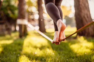 Foto op Canvas Slacklining is a practice in balance that typically uses nylon or polyester webbing. Girl walking on a slackline in a park during a sunset. Slack line © alexanderuhrin