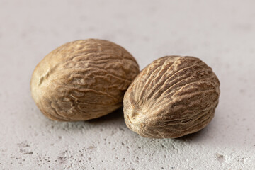Two whole nutmegs on a gray, porous surface. Close-up, copy space